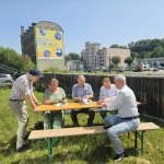 Bei sommerlichem Wetter unterzeichnen mehrere Vertreterinnen und Vertreter des Solarpfads Chemnitz-Erzgebirge an einem Biertisch im Freien eine Kooperationsvereinbarung; im Hintergrund sind ein großes Solarpfad-Banner an einer Fassade, eine überdachte PV-Parkplatzanlage sowie umliegende Gewerbebauten zu sehen.