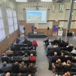 Beim 4. Energiedialog Chemnitz am 27. Januar 2026 präsentiert ein Referent auf einer Bühne im Industrieloft vor voll besetztem Saal das Projekt „Summit of Saxony“: Auf der Leinwand ist ein Aktivsonnenhaus-Gebäude der FASA AG zu sehen, während zahlreiche Fachgäste in Reihen sitzen und den Vortrag zur zukünftigen Energieversorgung in Sachsen verfolgen.