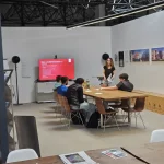 Im Rahmen der Berufsorientierungswoche „Schau rein!“ sitzen mehrere interessierte Schülerinnen und Schüler an einem langen Holztisch im Showroom der FASA AG, während eine Mitarbeiterin vorne steht und Ausbildungsberufe sowie duale Studiengänge vorstellt; auf einem großen Bildschirm im Hintergrund läuft eine Präsentation zum Beruf „Beton- und Stahlbetonbauer“, an der Wand hängen Referenzfotos von Bauprojekten.