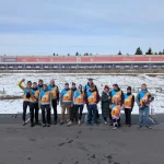 Gruppenfoto vom FASA-Sporttag in Oberwiesenthal: Eine größere Gruppe von Mitarbeitenden und Angehörigen steht auf der teilweise verschneiten Biathlonanlage, alle tragen orange-blaue Startnummernwesten, im Hintergrund sind die beschilderten Schießstände sowie Bandenwerbung der Sparkasse und weiterer Partner zu sehen.